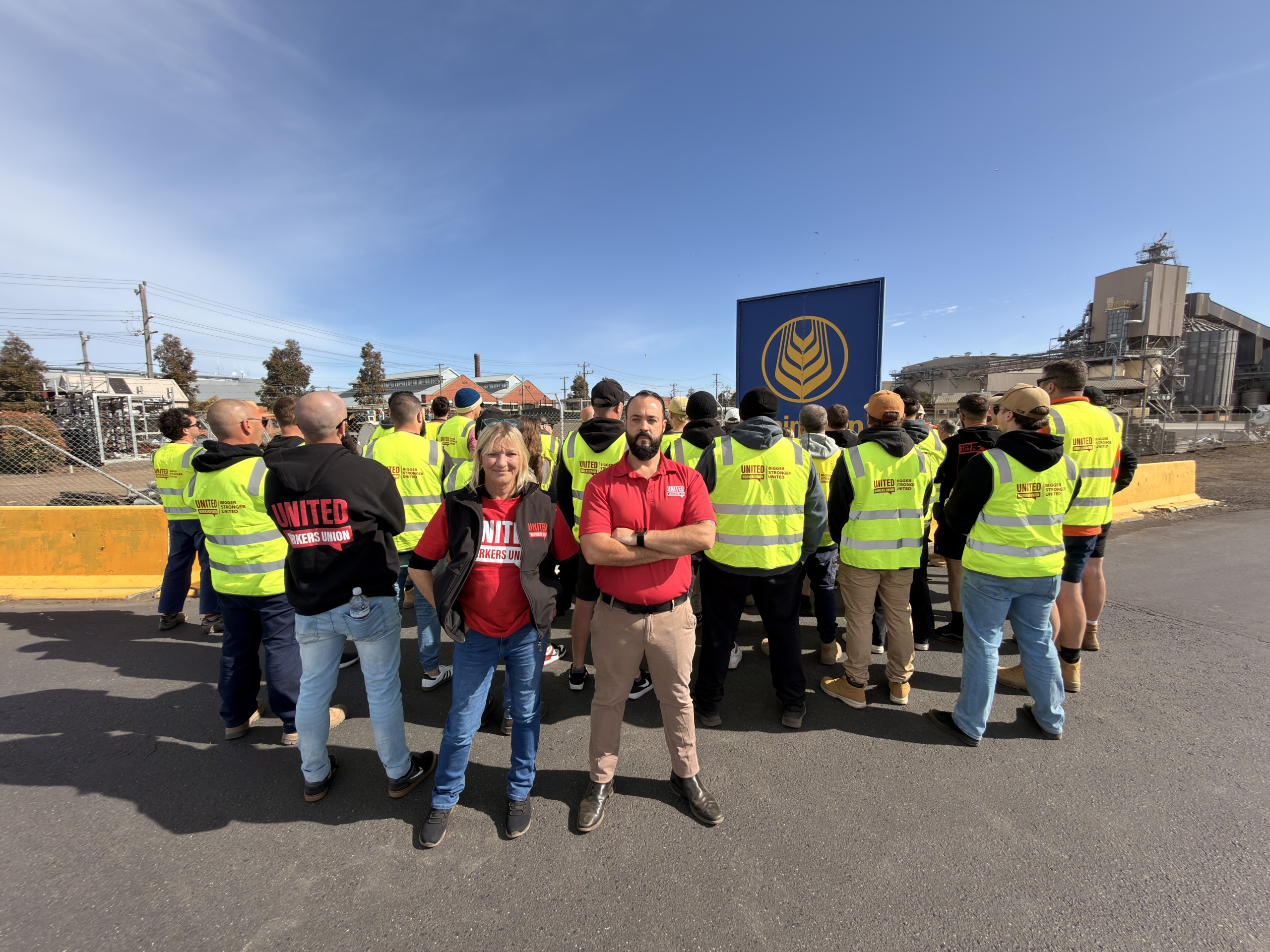 workers in hi-vis vests facing away from the camera with graincorp worksite behind them